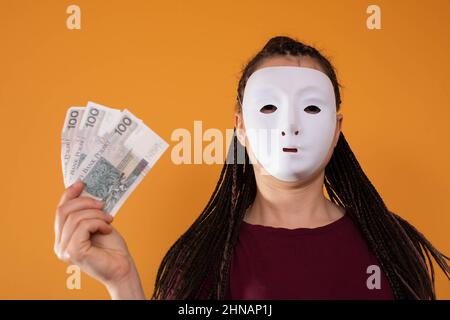 Una donna anonima si alza e tira la mano con banconote di carta con il valore facciale di cento zlotys polacchi. Nessuna faccia perché c'è una maschera Foto Stock