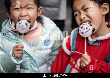 Wuhan, Cina. 15th Feb 2022. Due ragazze leccano la figurina di zucchero in simili a Pechino 2022 Winter Olympic Mascot Bing DWEN DWEN durante la celebrazione del Festival delle Lanterne che segna la fine delle celebrazioni del nuovo anno lunare. Credit: SOPA Images Limited/Alamy Live News Foto Stock