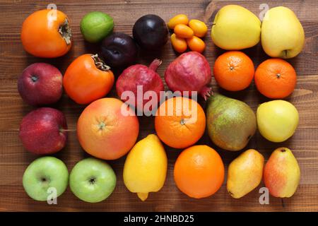 Diversi tipi di frutta su un tavolo di legno marrone. Vista dall'alto. Primo piano. Persimmoni, mele, prugne, melagrane, pere, arance, tangerini Foto Stock