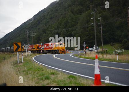 AICKENS, WEST COAST, NEW ZEALAND, 12 FEBBRAIO 2022: Un treno merci attraversa l'autostrada statale 73 ad Aickens sulla West Coast lungo il tragitto per la miniera di carbone di Stockton Foto Stock