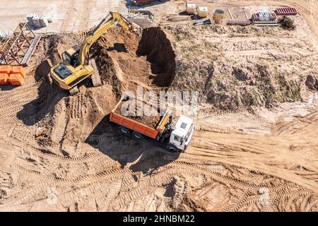 l'escavatore carica la sabbia in un camion in cantiere. vista dall'alto aerea da un drone. Foto Stock
