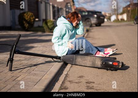 La donna caucasica è caduta da uno scooter elettrico e soffre di dolore. Foto Stock