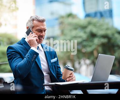 Può lavorare da qualsiasi luogo, hes il boss. Scatto di un bel uomo d'affari maturo in abbigliamento aziendale su una chiamata e utilizzando un portatile all'aperto durante il giorno Foto Stock