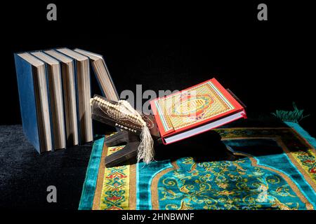 Corano su un placemat di legno in tappeto di preghiera con perle di preghiera su sfondo scuro Foto Stock