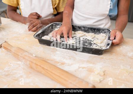 Mani di ragazzo che tagliano i biscotti dalla pasta arrotolata mentre cucinano la pasta per la cena di Natale Foto Stock