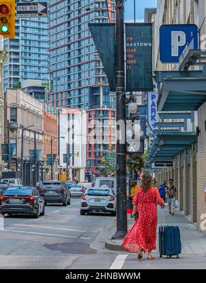 Tour turistico a piedi con valigia sulla strada della città urbana. Donna in abito rosso a piedi con i bagagli centro di Vancouver Foto Stock