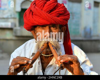 Anziano giocatore indiano di flauto algoza indossa un rosso Rajasthani turban (pagari) e suona i suoi tradizionali strumenti a vento di legno con due mani. Foto Stock