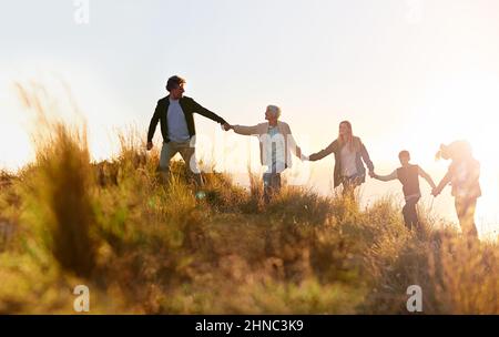 Il nonno è in testa. Scatto di una famiglia multi-generazionale che cammina mano in mano attraverso un campo al tramonto. Foto Stock