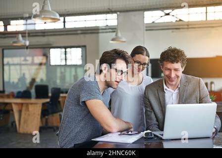 Il team di cui ci si può fidare per portare a termine il lavoro. Foto di colleghi che lavorano insieme su un notebook in un ufficio moderno. Foto Stock