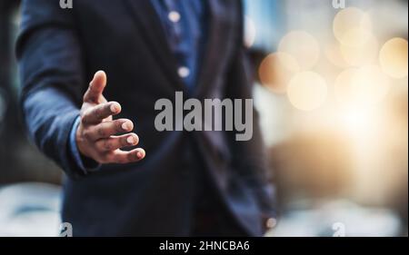 Lascia che questa fusione accada. Primo piano di un uomo d'affari irriconoscibile che estende una stretta di mano in città. Foto Stock