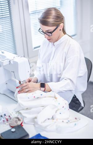 La donna fa i suoi propri vestiti seduti dietro la macchina da cucire. Foto Stock