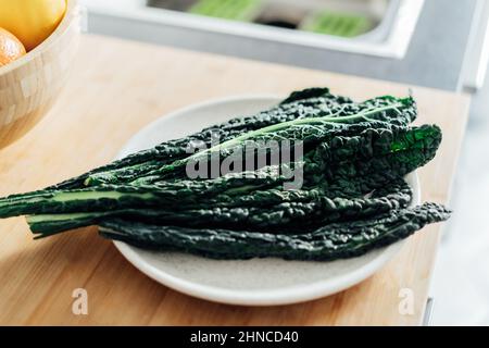 Foglie fresche di Cavolo Nero Kale su un piatto bianco e su un rustico fondo in legno sul tavolo di kintchen. Fase di cottura sana, pronta a preparare ve Foto Stock