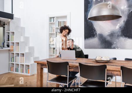 felice uomo afroamericano appoggiato sul ventre di moglie incinta in appartamento moderno Foto Stock