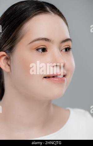 Donna sorridente con sindrome di Down che guarda via isolato su grigio Foto Stock