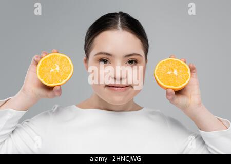 Donna sorridente con sindrome di Down che tiene arancione isolato sul grigio Foto Stock