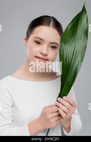 Donna bruna sorridente con sindrome di Down che tiene la foglia isolata sul grigio Foto Stock