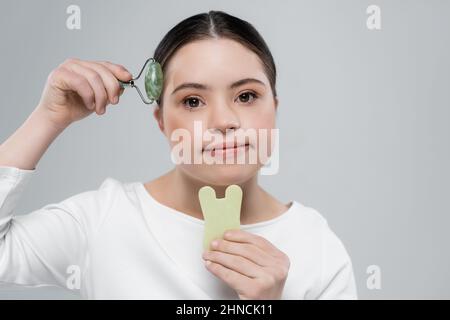 Donna con sindrome di Down che tiene jade rullo e pietra isolato su grigio Foto Stock