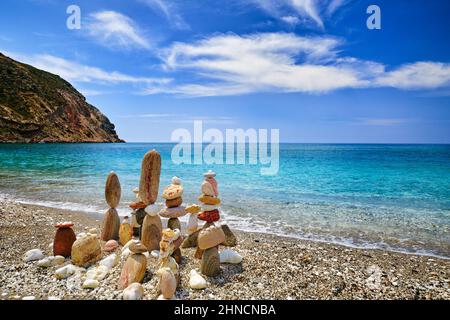 Gruppo di pietre equilibranti sulla spiaggia. Giorno di sole luminoso, atmosfera estiva, acqua di mare azzurra spruzzi su ghiaia costa, cielo blu e nuvole chiare Foto Stock