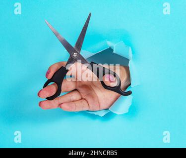 Mano donna con forbici in tutto di carta blu strappata sfondo Foto Stock