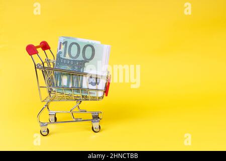 carrello da un supermercato con cento banconote da euro su sfondo giallo. Foto di alta qualità Foto Stock