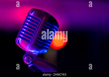 Microfono da palcoscenico classico. Oggetto illuminato con luce colorata. Sullo sfondo, una vista di luci sfocate sul palco. Foto Stock