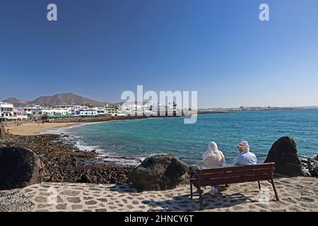 La coppia anziana si è seduta sul panchina guardando la vista di Playa Blanca, Lanzarote Foto Stock