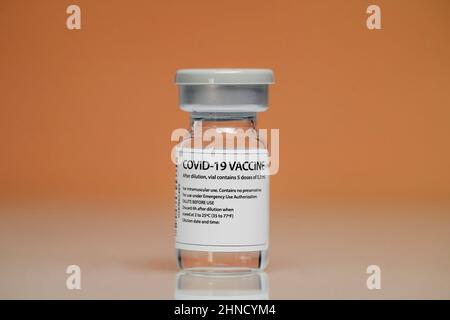 Flaconcino di vetro medico con vaccino contro il coronavirus posto su sfondo arancione Foto Stock