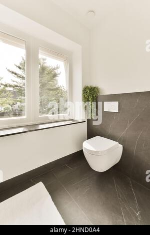 Interni di moderno bagno con WC bianco appeso su una parete piastrellata vicino alla finestra Foto Stock