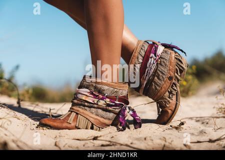 Vista laterale del raccolto anonimo viaggiatore femminile in stivali eleganti in piedi sulla costa sabbiosa in giornata di sole contro il cielo blu Foto Stock