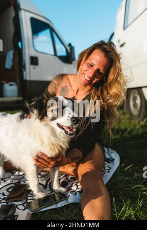 Positiva donna proprietario abbracciando carino peloso australiano Shepherd cane con muso avvistato mentre seduto su strada soleggiata il giorno d'estate Foto Stock