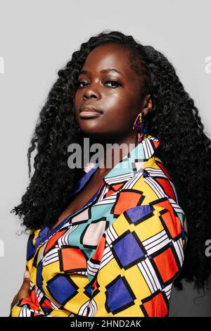 Vista laterale ritratto di Afro American Woman con capelli ricci e abiti colorati luminosi su sfondo bianco Foto Stock