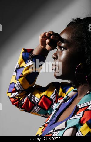 Vista laterale di Crop African American Woman in camicia colorata in piedi con braccia sollevate e guardando lontano Foto Stock