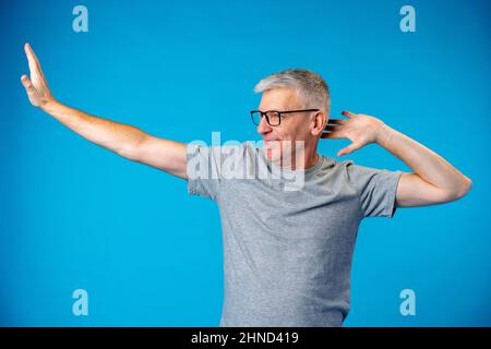 Uomo dai capelli grigi di mezza età che balla e si diverte sul backgorund blu Foto Stock