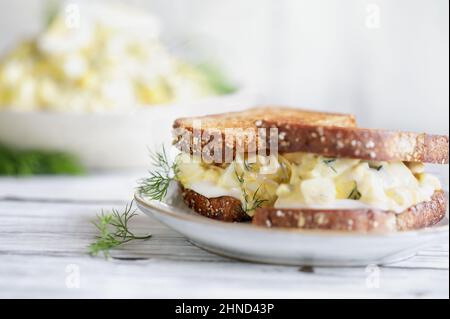 Estratto di un sandwich di insalata di uova con aneto fresco su un rustico tavolo di legno. Messa a fuoco selettiva estrema con primo piano e sfondo sfocati. Foto Stock