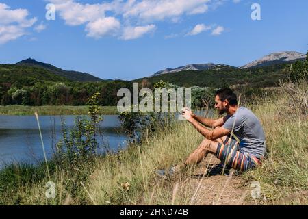 Uomo solo sulla riva del lago e scatta una foto sul suo smartphone Foto Stock