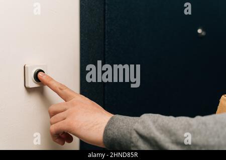 Primo piano di un uomo irriconoscibile premendo pulsante campanello all'ingresso dell'edificio di appartamenti. Venditore, ospite o visitatore dietro la porta. Foto Stock