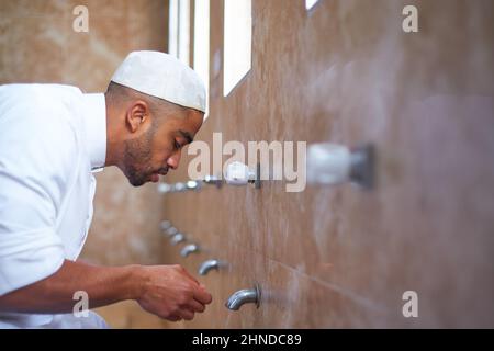 Un uomo musulmano che pulisce il viso con acqua nel bagno Foto Stock