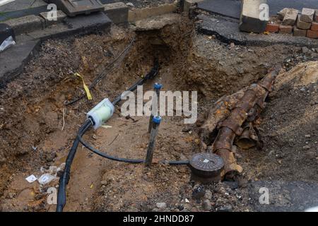 Scavato il marciapiede rivelando i fili in tubi di protezione. Costruzione di linee elettriche o cavi per telecomunicazioni, costruzione di rete ottica informaz Foto Stock