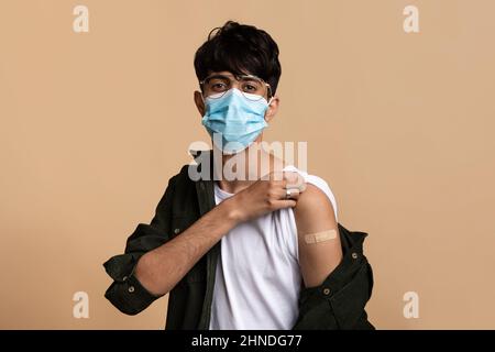 Giovane uomo indiano in maschera di faccia che mostra che è stato vaccinato Foto Stock