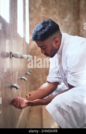 Un giovane musulmano pulisce le mani con acqua nel bagno Foto Stock