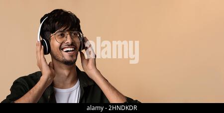Primo piano di un ragazzo arabico positivo che utilizza cuffie wireless, spazio di copia Foto Stock