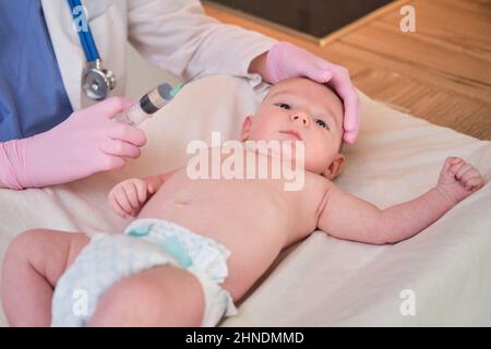 Il medico usa una siringa per iniettare un neonato. Un'infermiera in uniforme si prepara a vaccinare un bambino Foto Stock