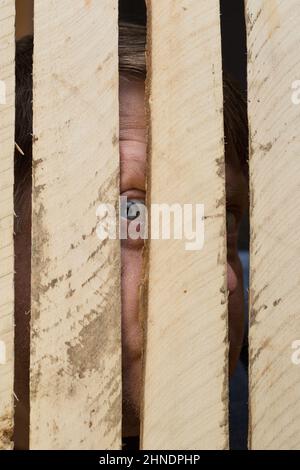 Un uomo guarda attraverso una crepa in una recinzione di legno. Il concetto di curiosità. Foto Stock