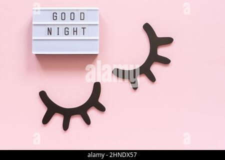 Testo scatola luminosa buona Notte e decorativo legno ciglia nera, occhi chiusi su sfondo di carta rosa. Scheda di saluto Concept Sweet Dreams Top View Crea Foto Stock