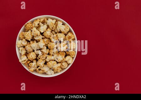 popcorn al caramello in ciotola rossa con spazio di copia per testo, primo piano, snack dolci, popcorn al caramello per guardare film Foto Stock