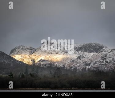 La luce invernale bassa illumina i Langdale Pikes ricoperti di neve Foto Stock