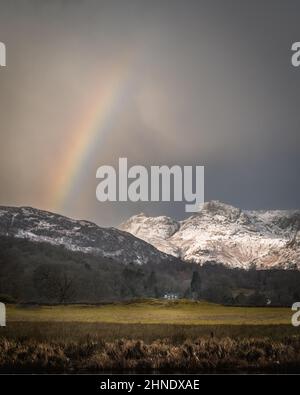 Superba luce invernale sui Langdale Pikes ricoperti di neve con arcobaleno Foto Stock