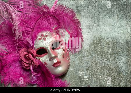 Maschera di Carnevale fatta a mano a venezia. La maschera è fatta di papier-mâché e rappresenta il volto di una donna, è di colore rosa e decorata con piume. Foto Stock