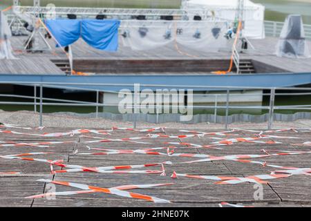 Panchine in legno vuote, auditorium teatro all'aperto chiuso con nastro rosso e bianco, palco chiuso su sfondo acqua Foto Stock