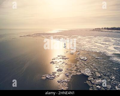 L'atleta uomo sta pedalando sul sup board nel lago con ghiaccio in inverno. Colpo di drone aereo. Concetto di sport estremi all'aperto Foto Stock